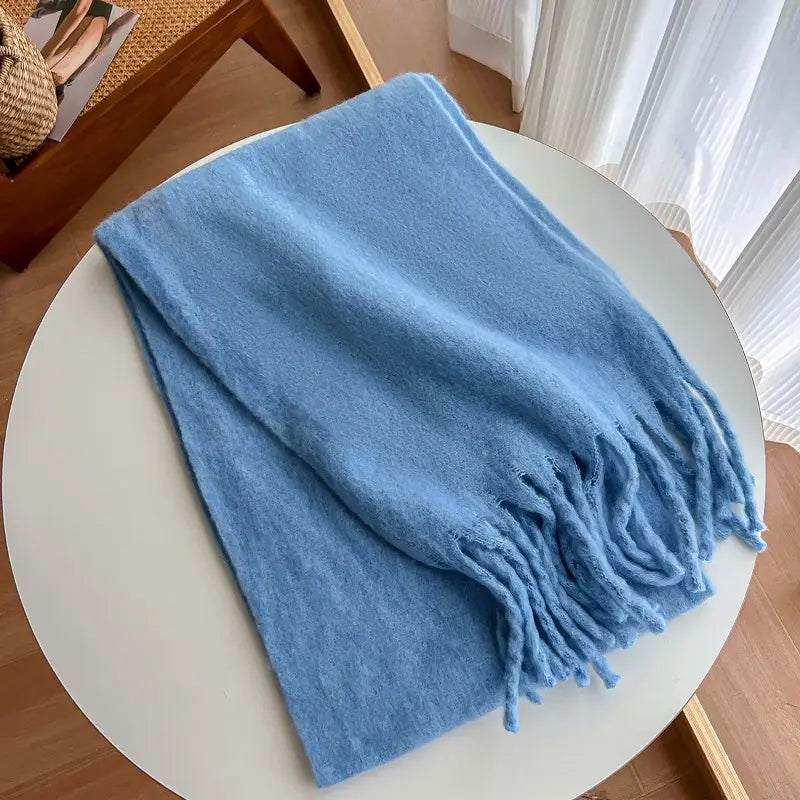 Bufanda de cachemir de invierno rosa para mujer, presentada como una bufanda tejida azul claro suave con bordes con flecos, doblada con esmero sobre una mesa blanca.