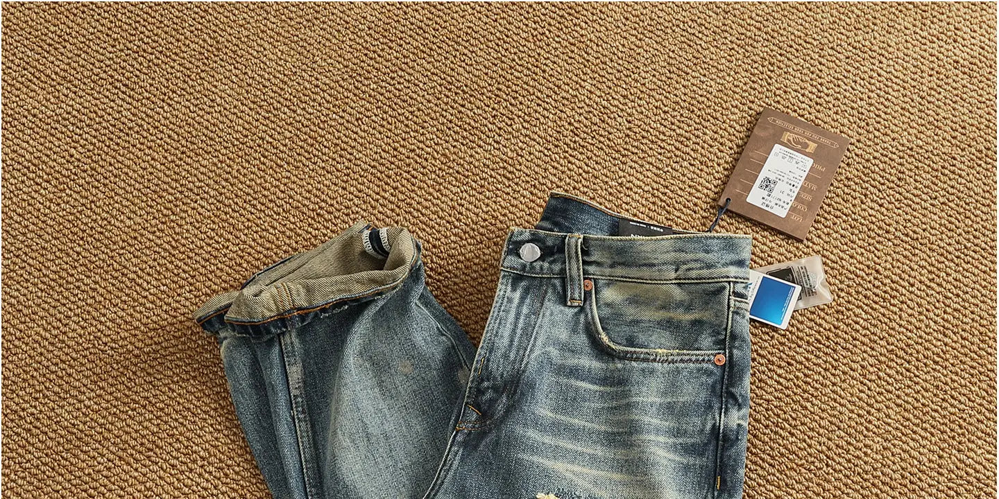 A pair of medium-wash distressed patchwork denim jeans for men with rolled cuffs.