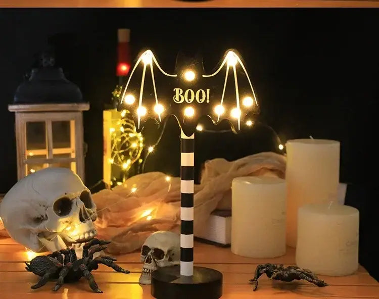 Eine schwarze und weiße, gestreifte LED-Nachtlampe im Fledermaus-Design mit leuchtenden Glühbirnen, die die Flügel bilden, sowie „Boo“-Text in der Mitte, als wasserdichte Halloween-Dekoration ausgelegt.