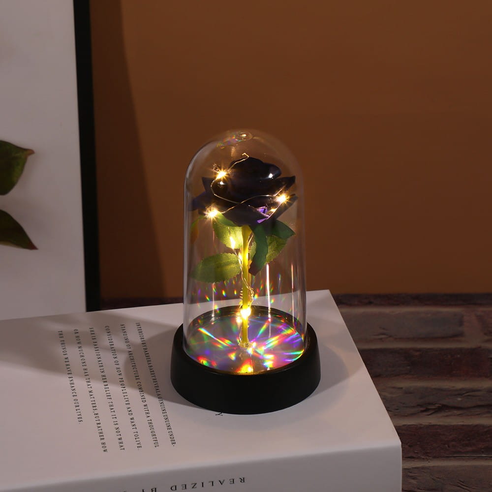 Une rose noire enfermée dans un dôme en verre transparent avec des lampes à DEL internes projetant des reflets colorés sur la base dans le cadeau de fleur lumineux en dôme de rose éternelle.
