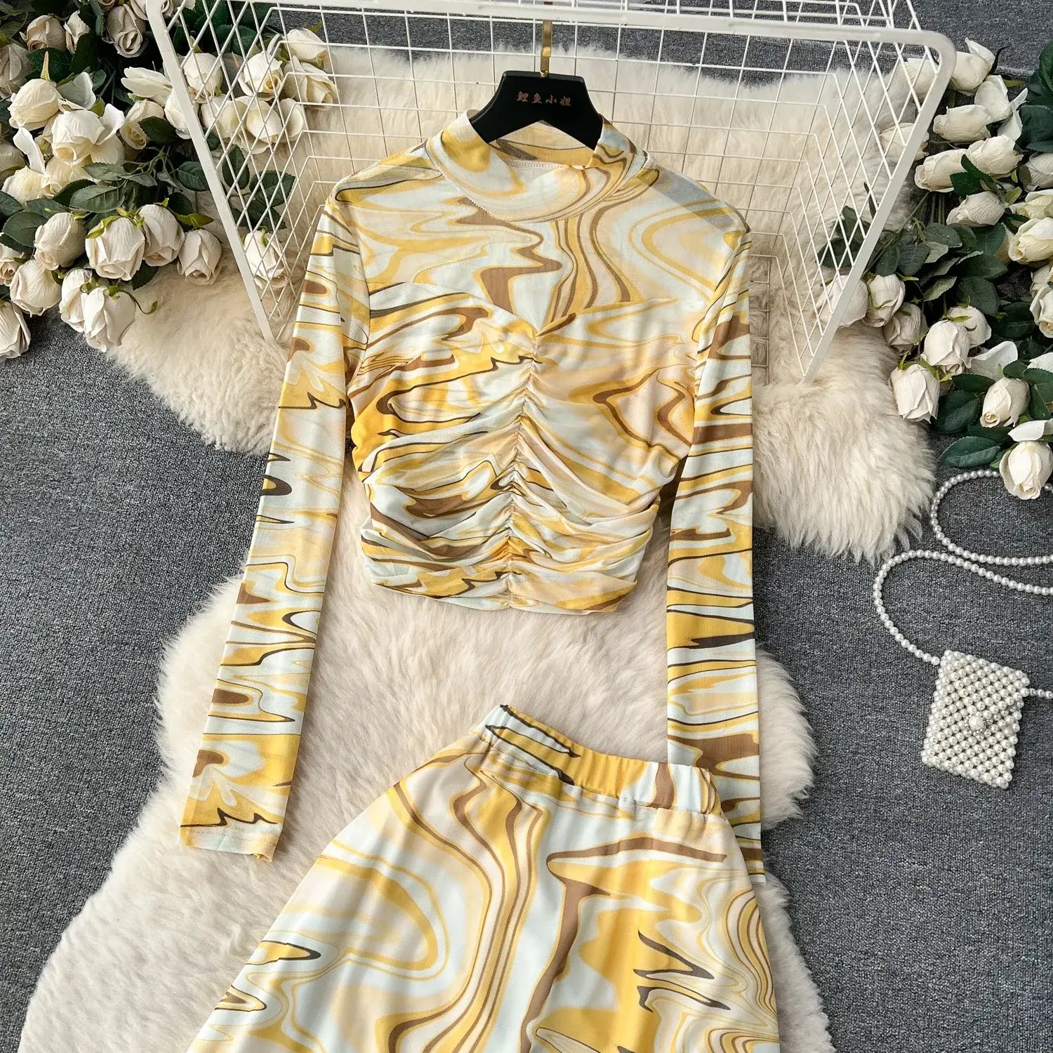 yellow and white marbled long-sleeve top with ruched front and elastic closure type displayed on black hanger as part of two piece mesh skirt set marble print