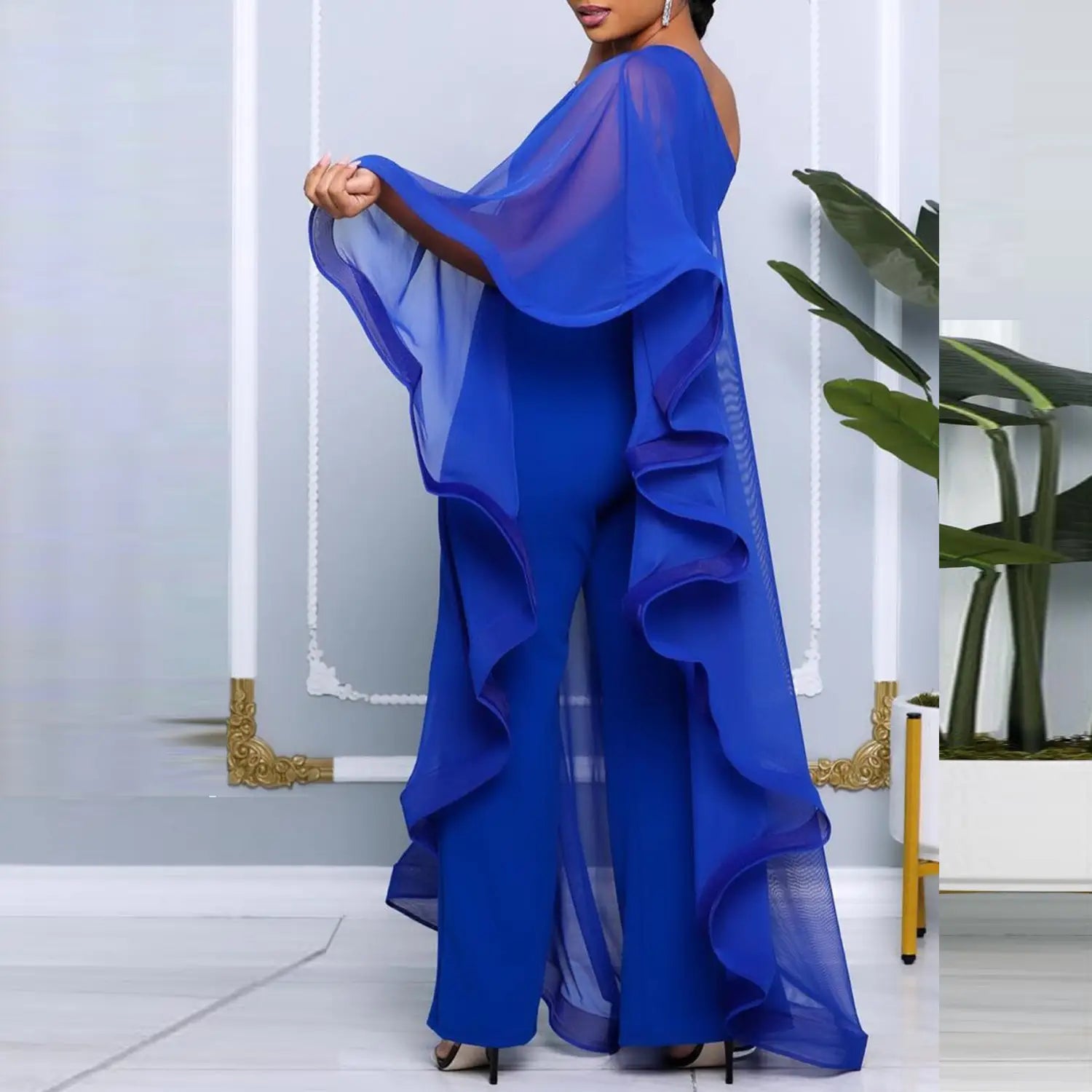 Ein leuchtend königsblaues, transparentes Rüschen-Cape-Top mit weiten Ärmeln, getragen über passenden hoch sitzenden Hosen, im Kontrast zum eleganten weißen Chiffon-Jumpsuit mit einseitiger Schulter und Rüschen.