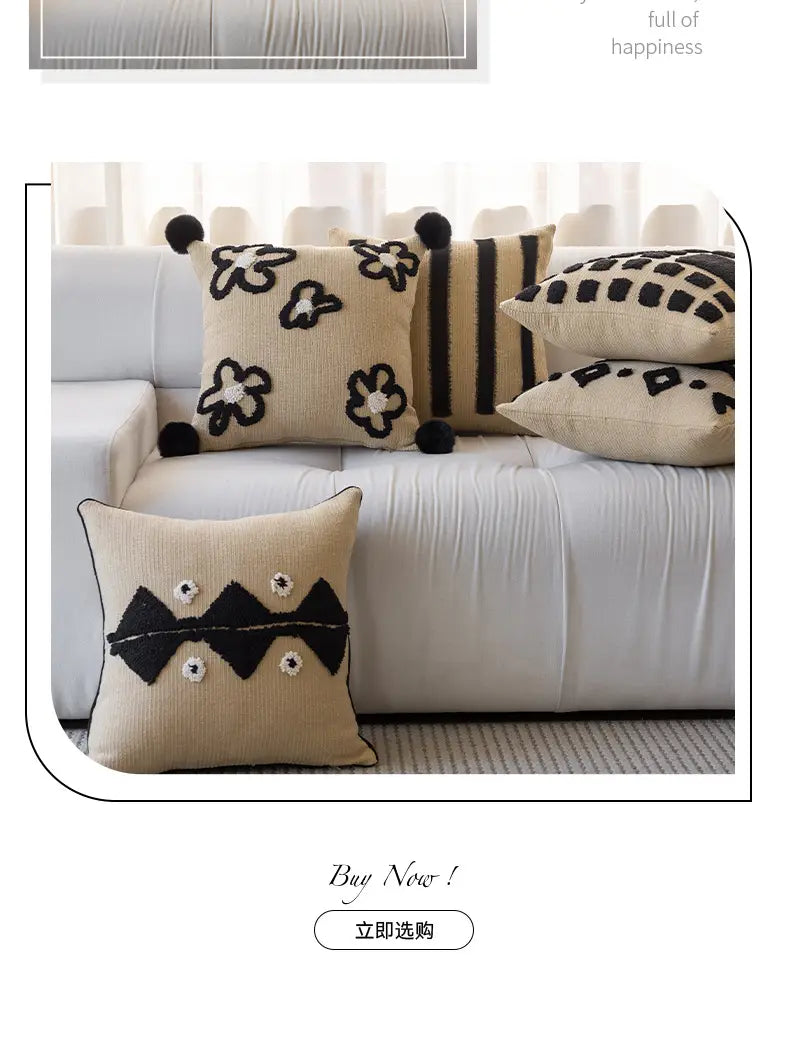 Housse de coussin bohème beige, avec des motifs floraux et géométriques brodés en noir, agrémentés de pompons moelleux, pour la décoration du salon.