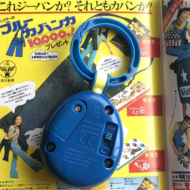 Blue plastic Tamagotchi electronic virtual pet keychain from the 90s with a circular handle and oval body featuring Bandai Meds 2019 printed text on the back side.