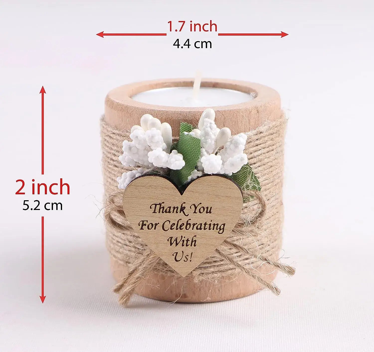 Un bougeoir rustique en bois, en forme de petite bougie chauffe-plat, avec une finition naturelle enveloppée de cordelette et orné de fleurs artificielles blanches, ainsi qu’une étiquette en bois en forme de cœur indiquant « merci de célébrer avec nous » pour des cadeaux d’invités de mariage.