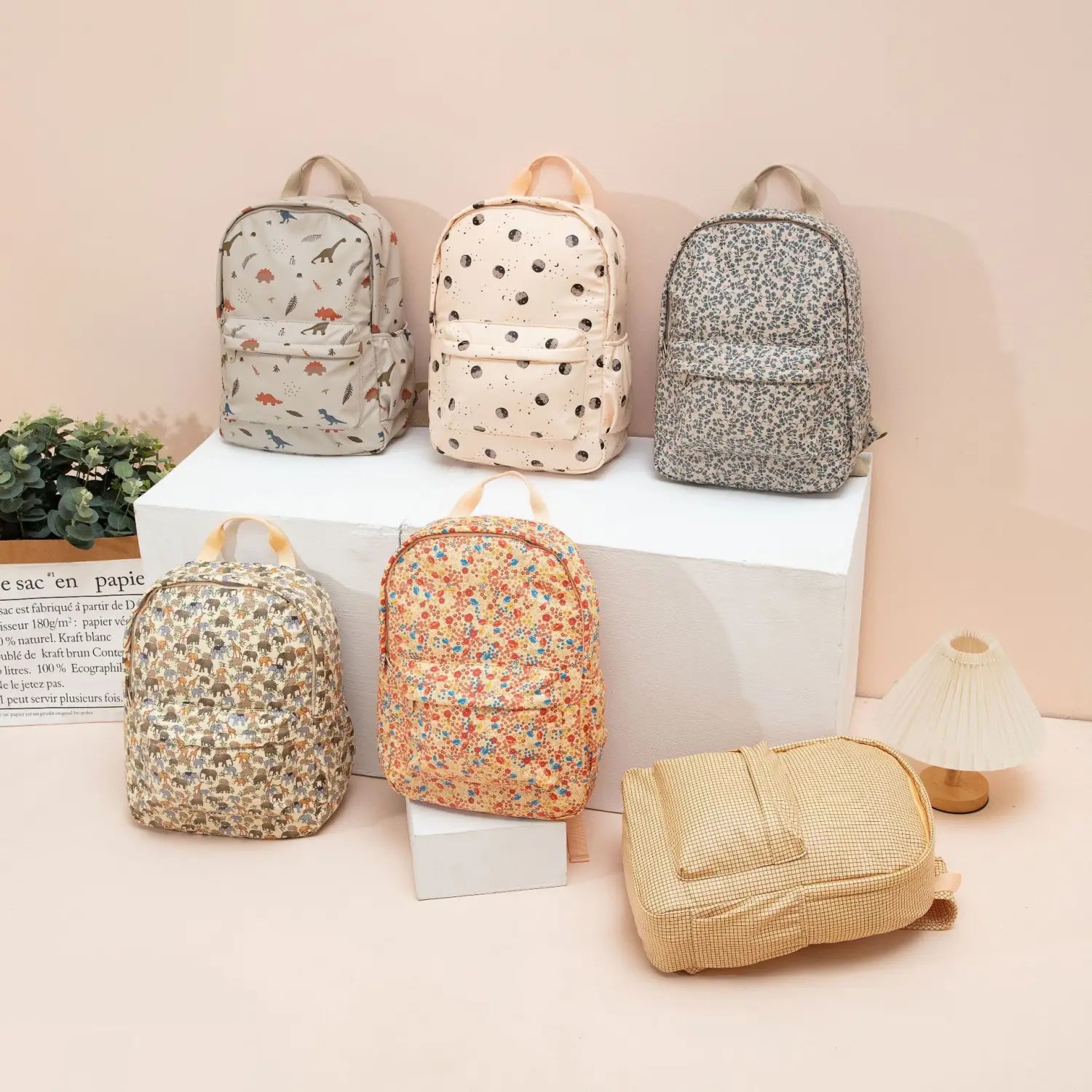 Un sac à dos beige en raphia tissé pour enfants à thème dinosaure, avec un tissage de fibres naturelles texturé et une fermeture de rabat simple, adapté comme sac d’école pastel.