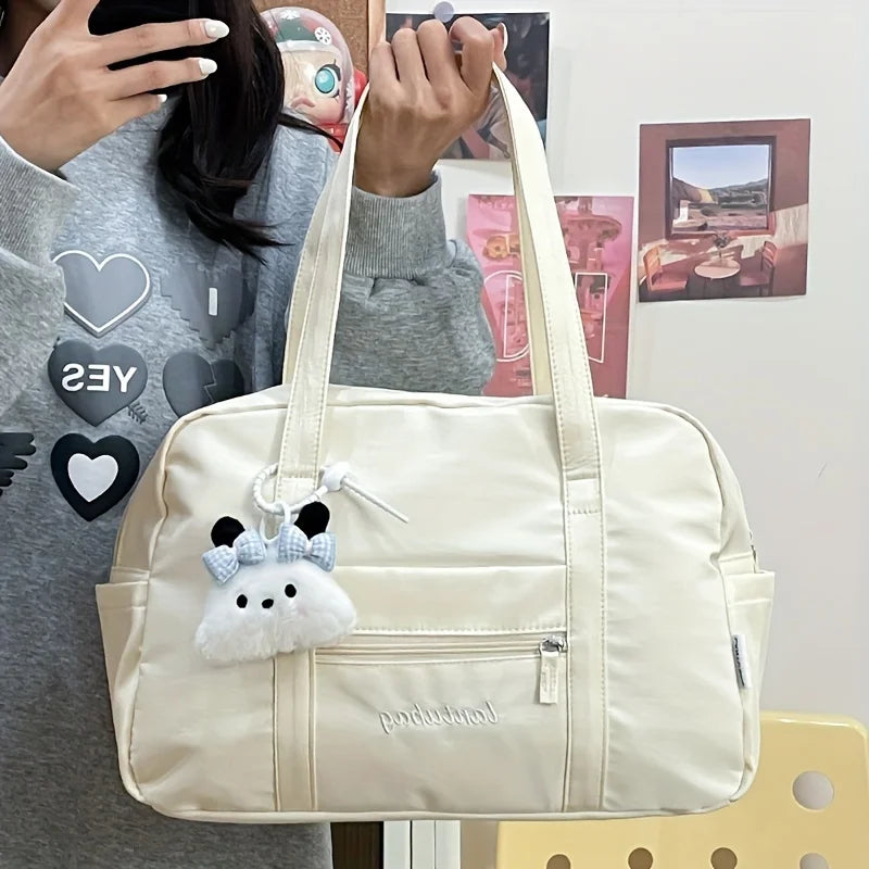 Bolsa de viaje tote de nailon acolchado color crema con textura suave y un llavero de panda de peluche colgando de la asa.