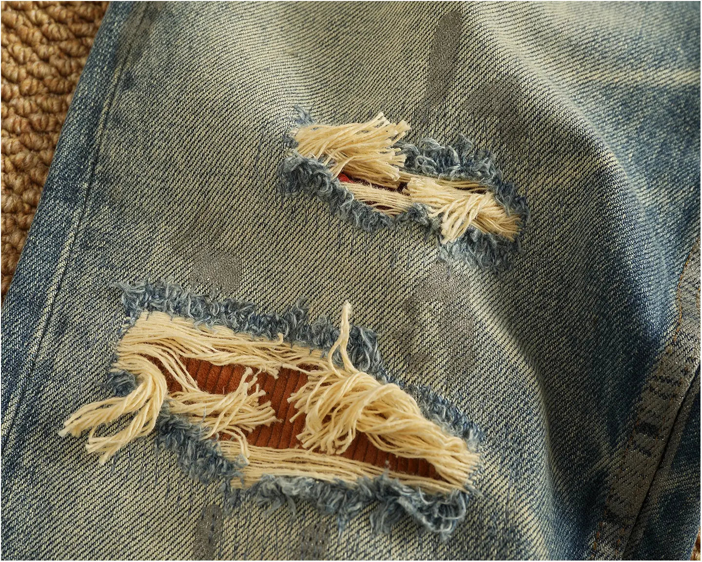 Distressed patchwork denim jeans for men in blue with frayed ripped patches revealing brown inner lining.