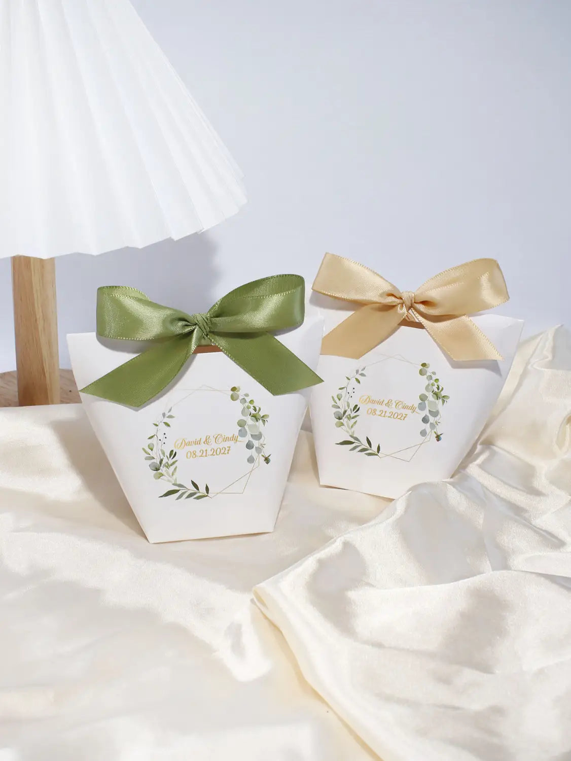 Deux boîtes à faveur de mariage florales en papier blanc personnalisables, chacune ornée d’un nœud en satin vert ou doré et de motifs délicats de couronne feuillagée assortis, pour célébrations de mariage, 50 pièces