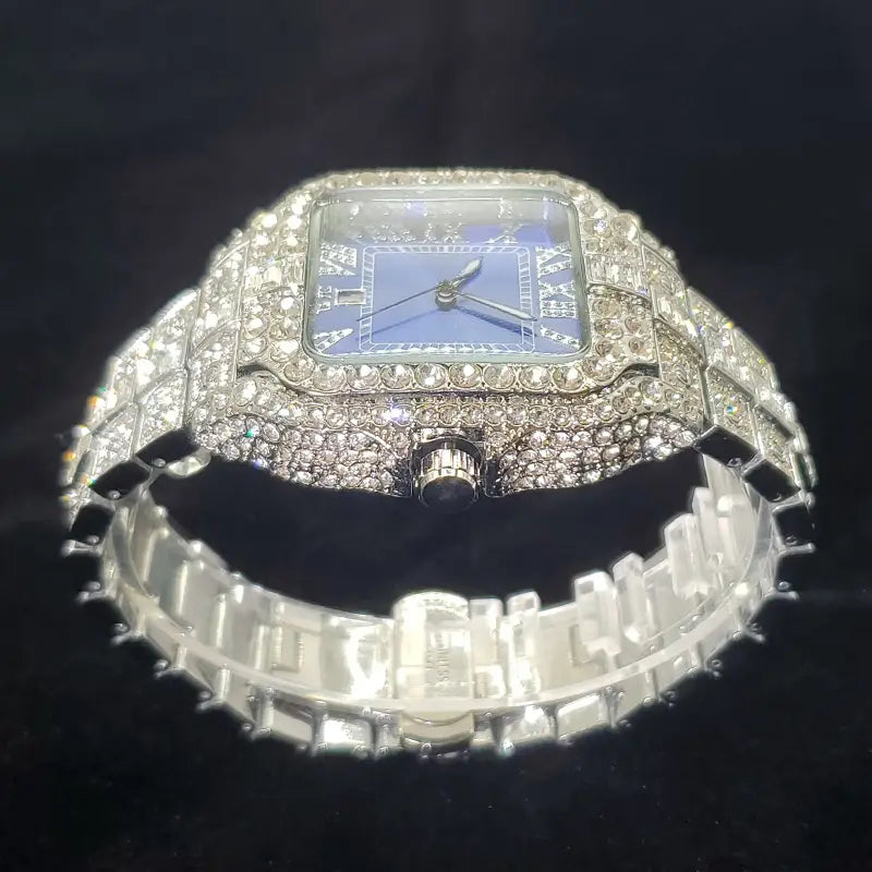 A luxurious iced out diamond square watch for men with a silver case, blue dial, and sparkling clear crystals encrusted along the bezel and integrated bracelet.
