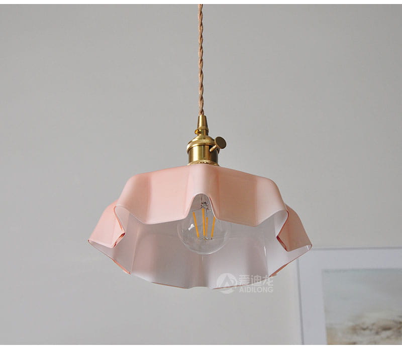 Un luminaire délicat suspendu à jupe florale en verre rose avec une conception d’abat-jour à pétales cannelés et une tête de lampe en cuivre montrée depuis l’avant.