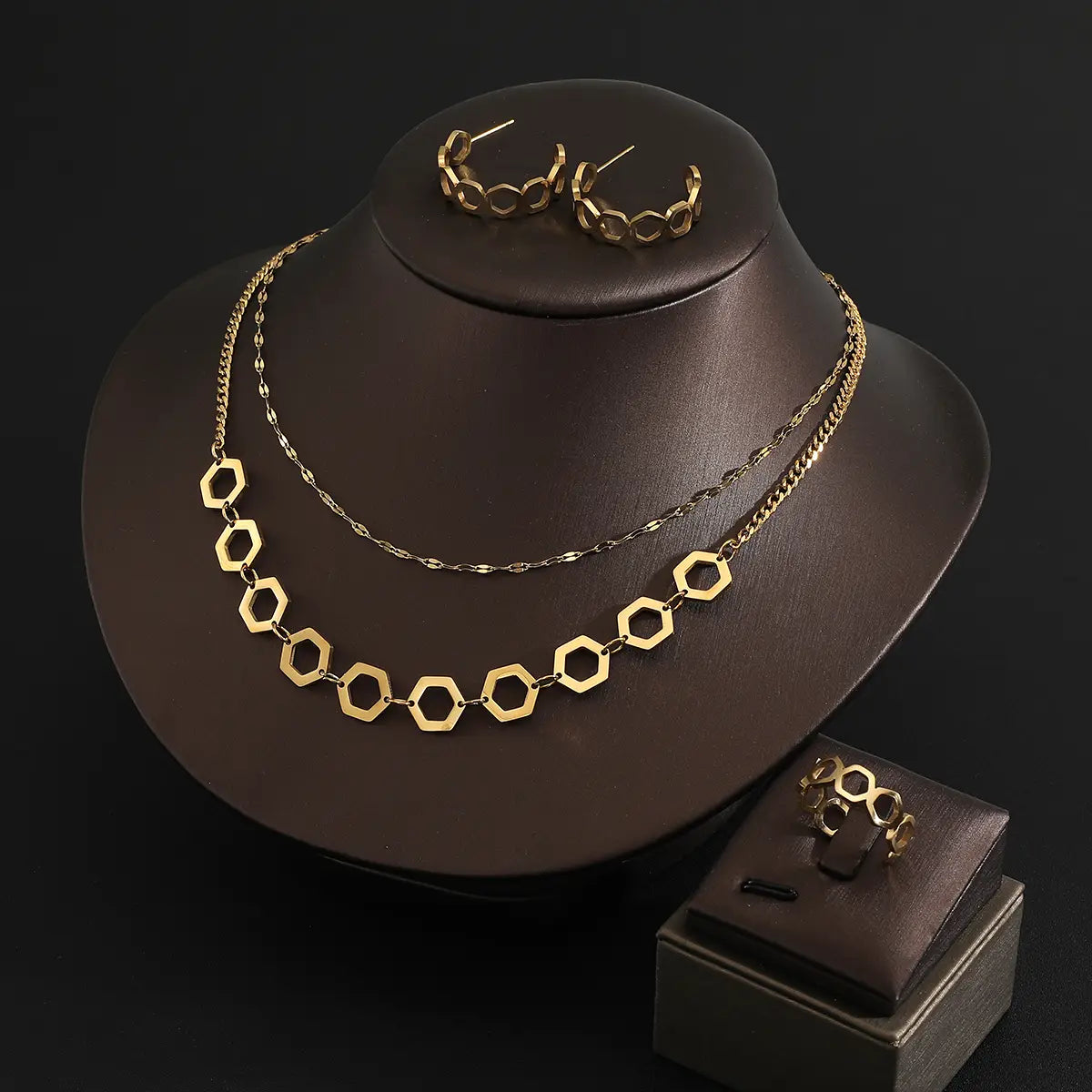 juego de joyería de acero inoxidable color dorado para mujeres, con un collar con cadena hexagonal de tono dorado, diseño de doble capa y segmentos alternados de eslabones sólidos y abiertos.