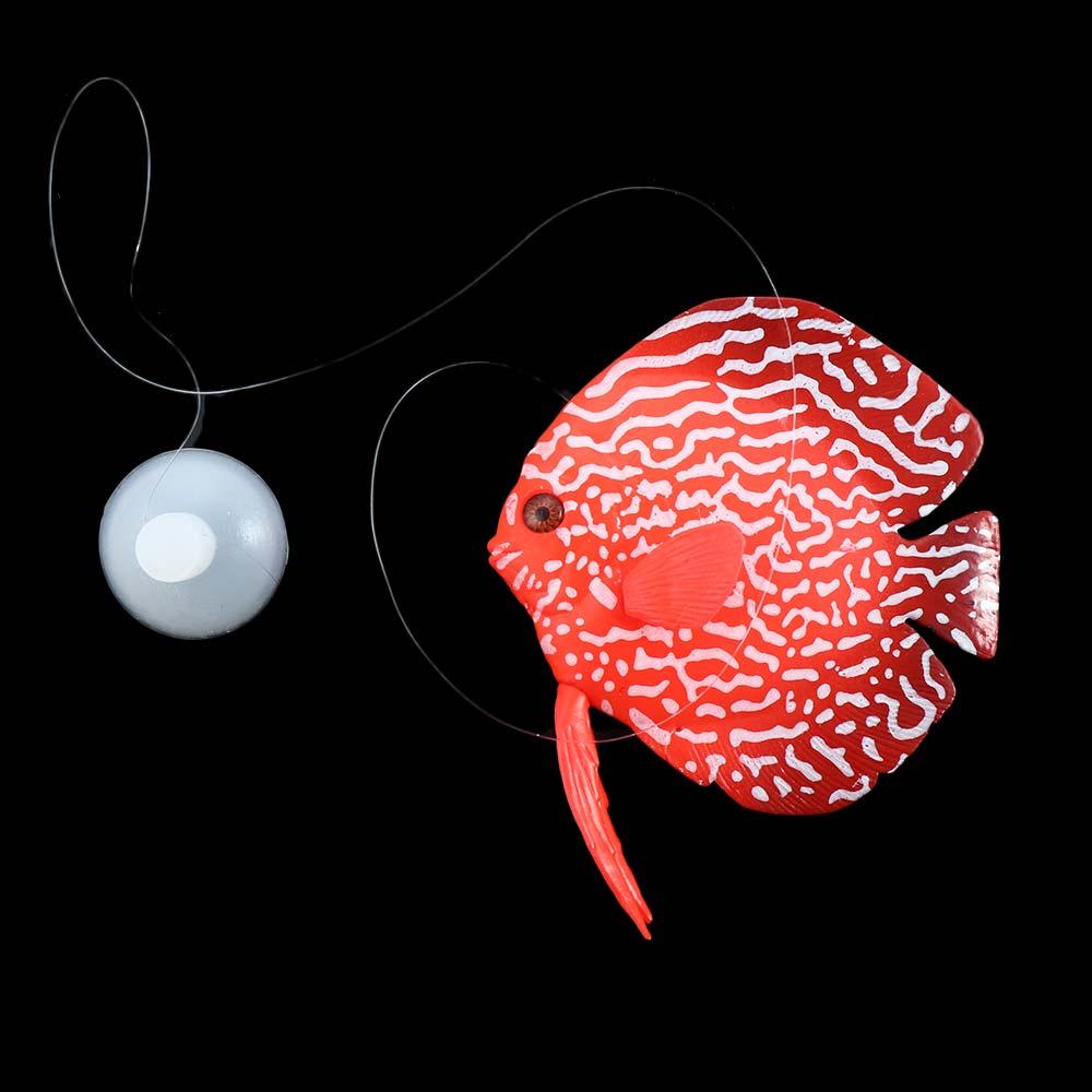 Eine künstliche Silikon-Aquarienzierde mit einem roten und weißen gemusterten Plastiktier in Form eines Zackenbarschs (Diskus) mit einem durchsichtigen Band, das an seinem Schwanz befestigt ist.
