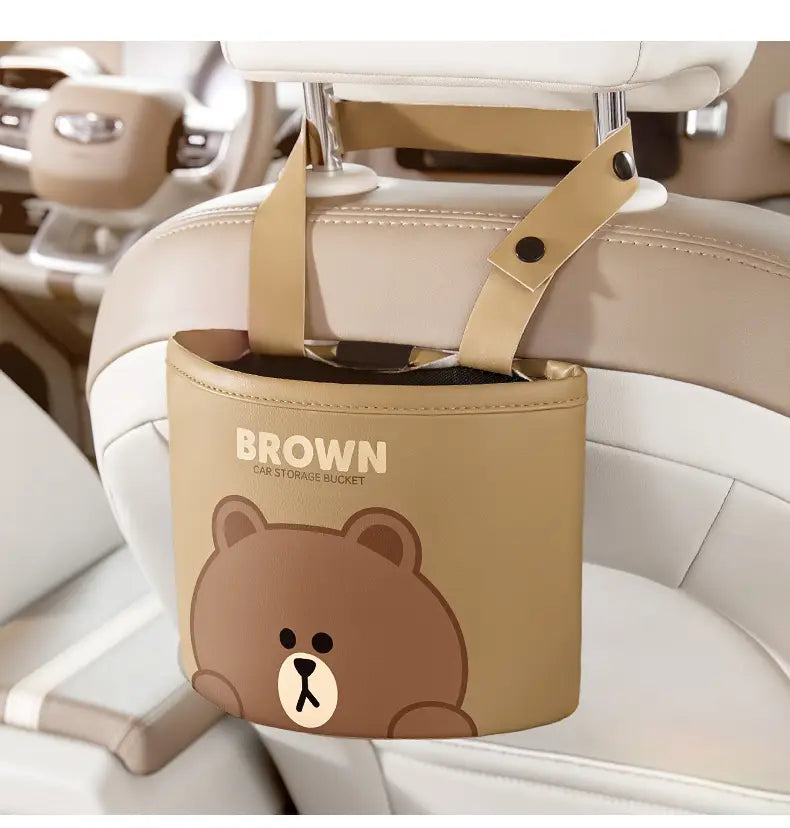 Cubo cilíndrico de almacenamiento para coche color beige, con rostro de osito marrón y marca en color marrón, fabricado en piel sintética, con correas de imitación de cuero para el montaje en el reposacabezas, diseñado como bolsa organizadora del asiento trasero.