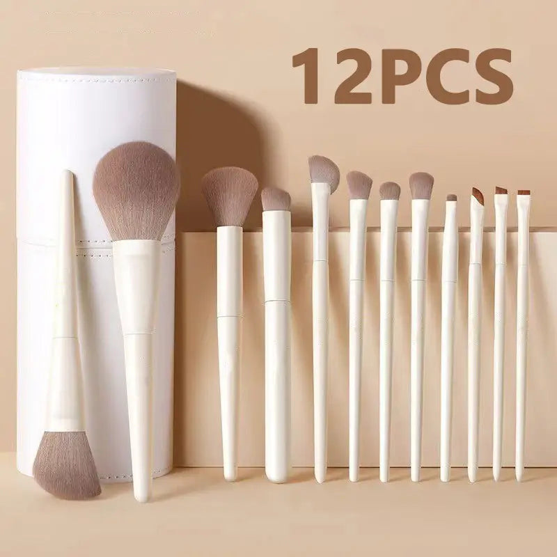 Ensemble de maquillage de 12 pinceaux blancs et dorés, doté de poils beige doux et de manches blancs disposés avec soin à côté d’un étui cylindrique assorti