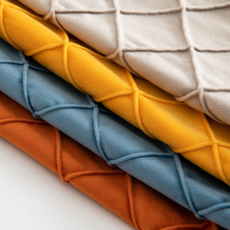 panneaux de tissu matelassé empilés en jaune, bleu et orange vibrants, avec une surface texturée et douce, complètent une housse de coussin en velours gris avec pompons, recevant des retours positifs pour des housses de coussin.