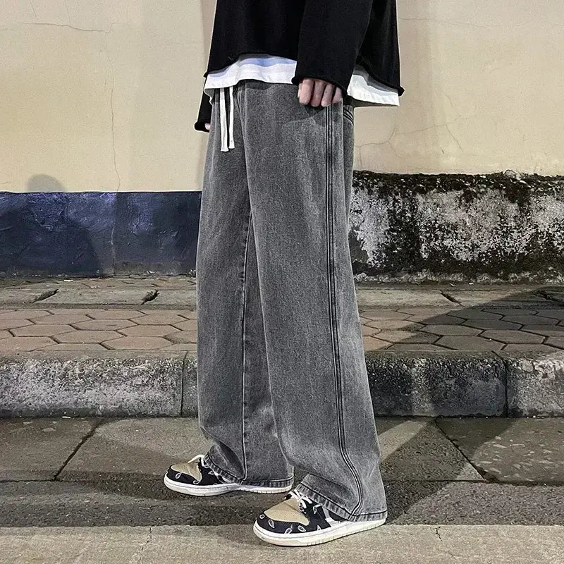 Jeans en denim gris à jambes larges pour hommes, avec une coupe streetwear coréenne ample et des cordons de serrage blancs à la taille.