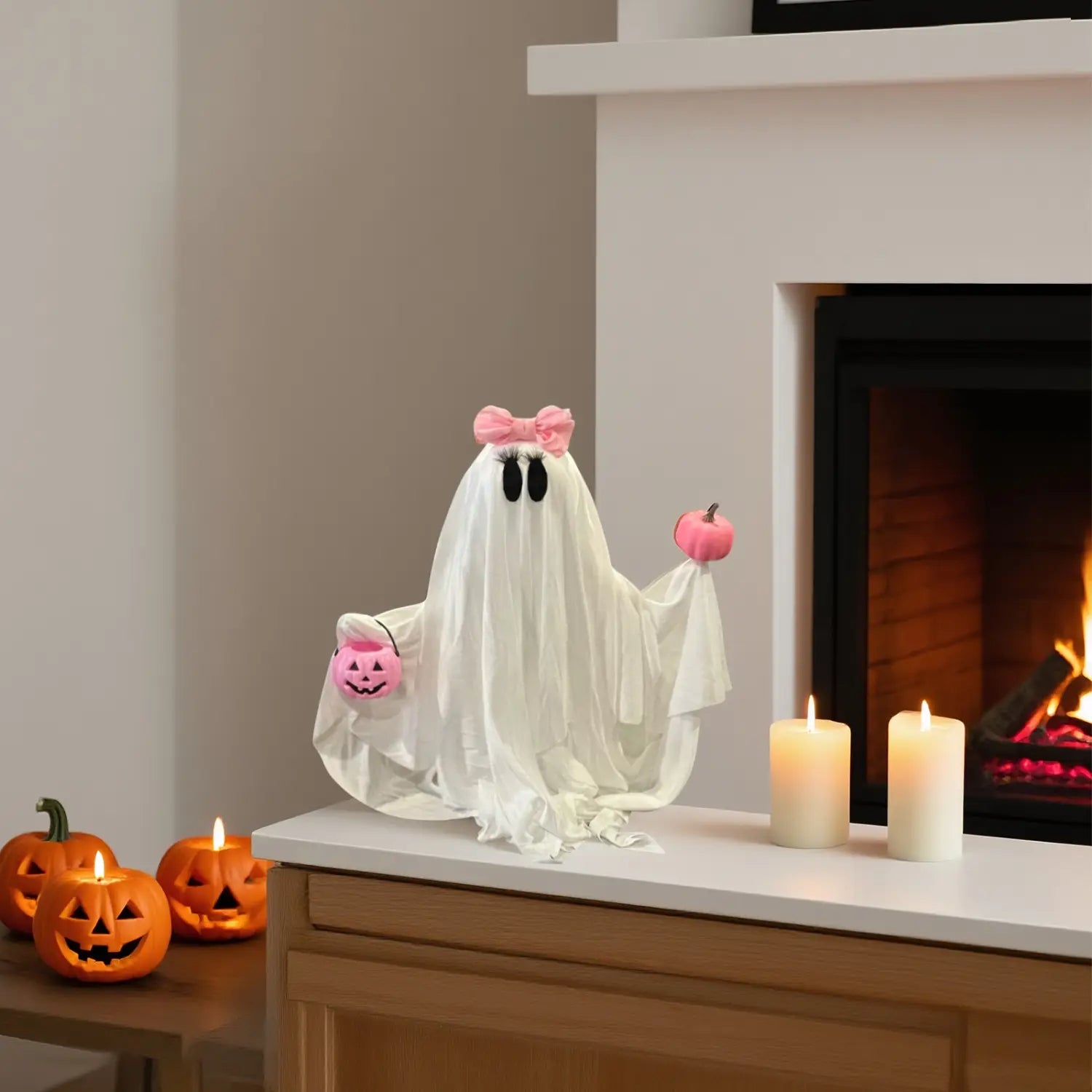eine weiße Stoff-Geister-Halloween-Tischdekoration mit einer rosa Schleife auf dem Kopf, die zwei kleine Kürbisse hält.