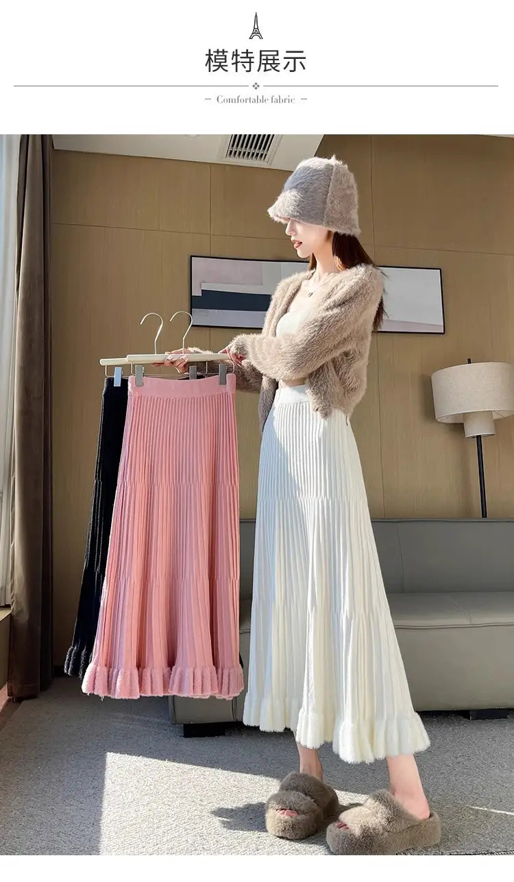 Une jupe mi-longue en maille blanche, souple, avec taille haute, plis et ourlet parapluie évasé, présentant de légères nervures verticales