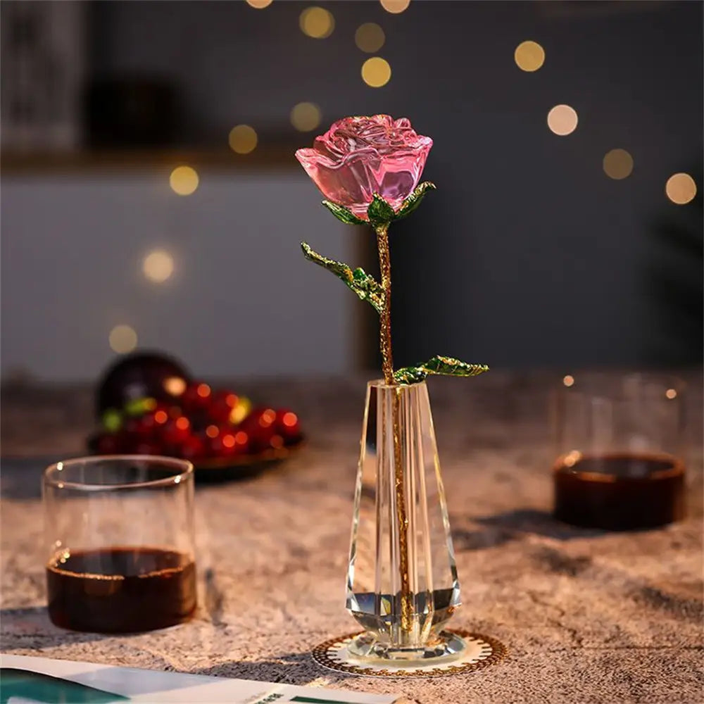 A translucent pink crystal rose with a gold-leafed stem and leaves displayed in a faceted clear glass vase as a crystal glass rose gift for Valentine’s Day.