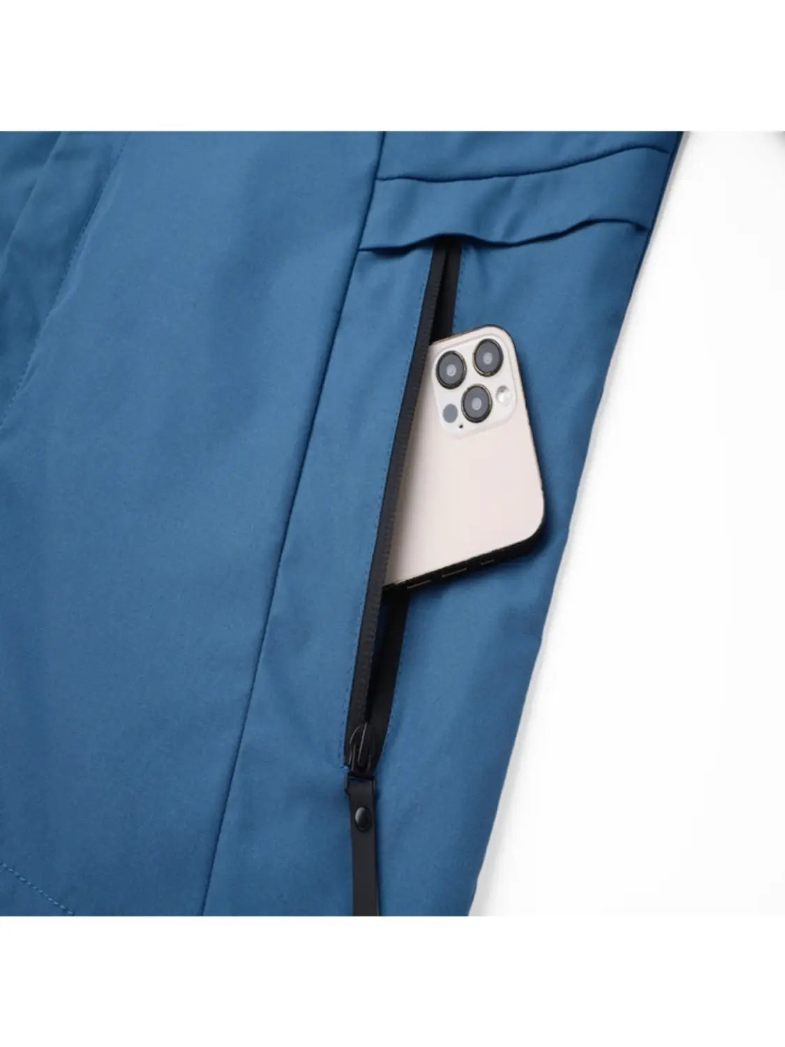 A sleek silver iPhone with a triple-camera system peeking out from the zipper of a blue quilted men off road hooded jacket windproof casual outerwear.