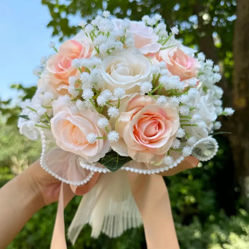 A delicate white silk rose wedding bouquet with peach and white artificial roses accented with babies breath tied with a sheer lace ribbon.