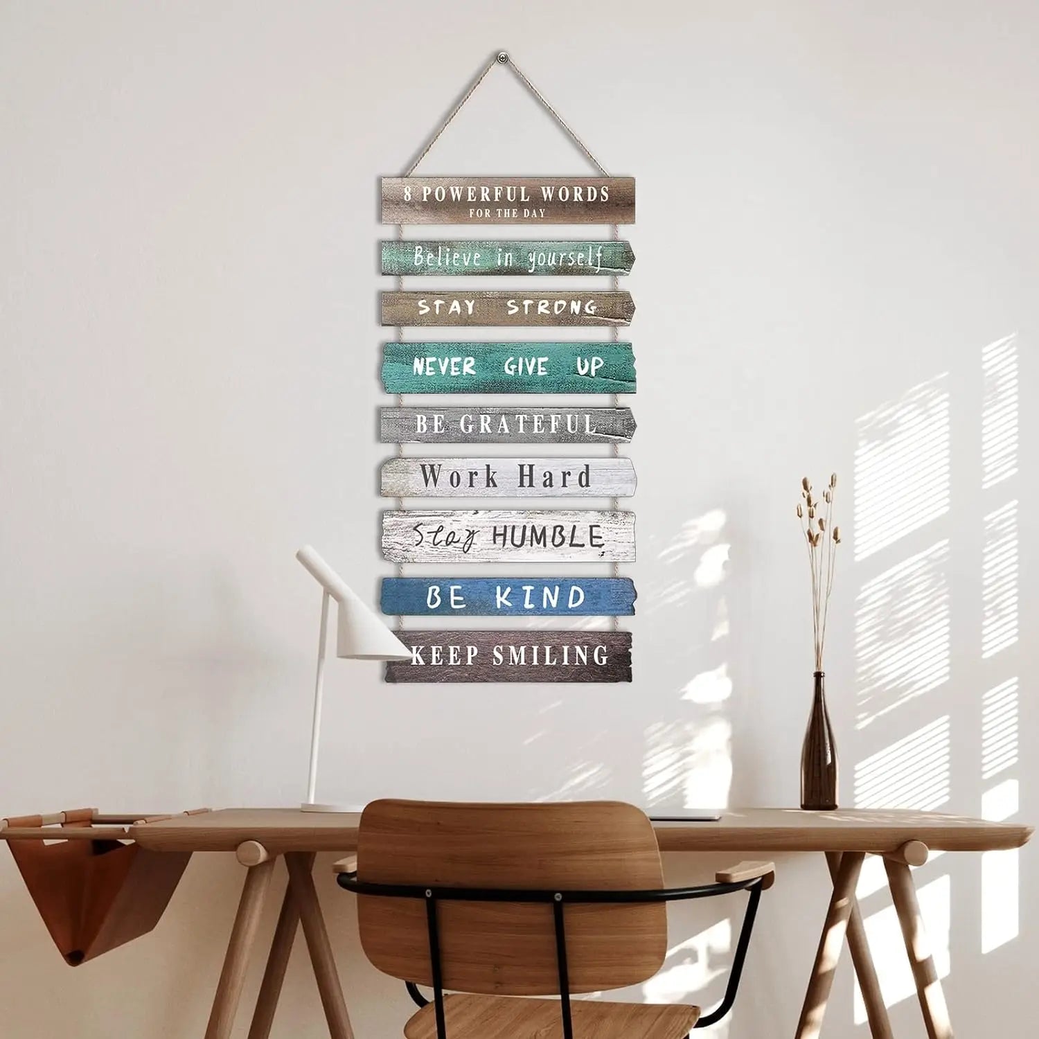 A rustic wooden wall art with varied colored motivational phrases and textures hung by a metal hanger for inspirational decor.