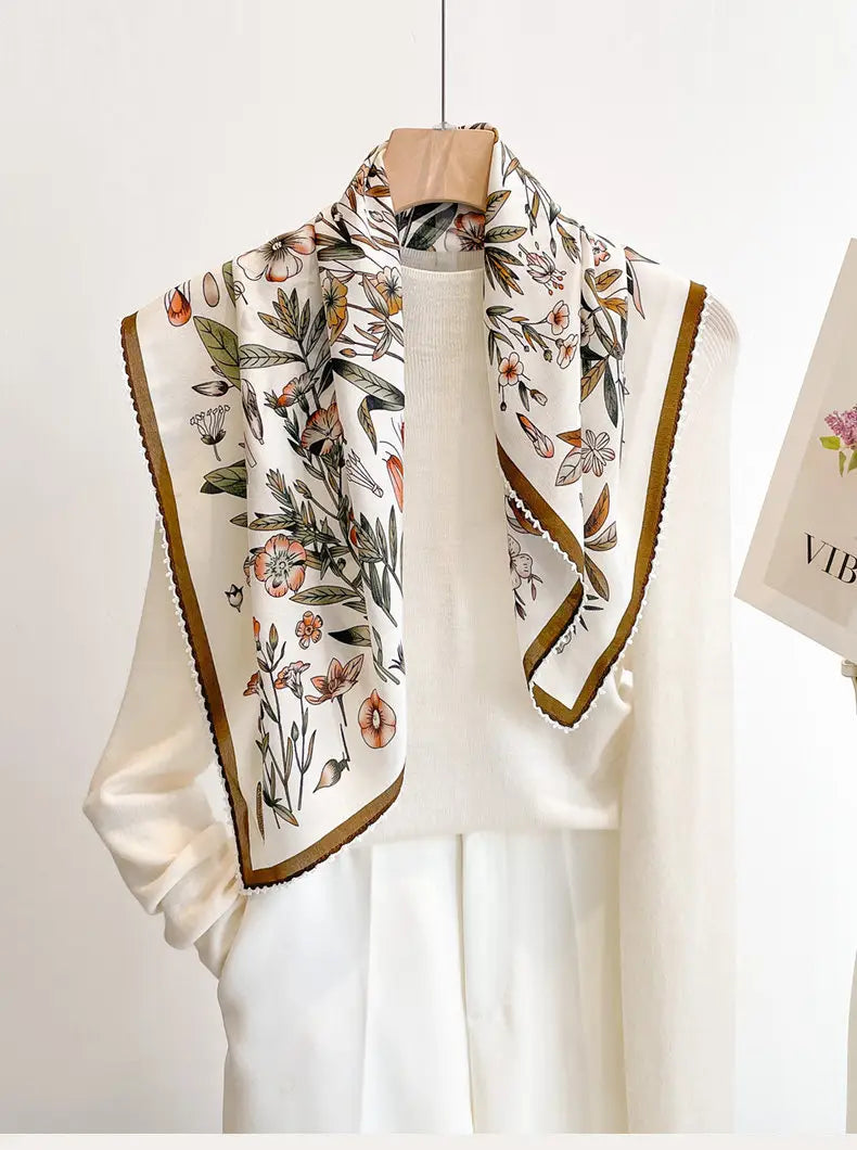 A delicate ivory silk floral square scarf featuring a botanical print of soft pink and green flowers with a contrasting mustard yellow border.