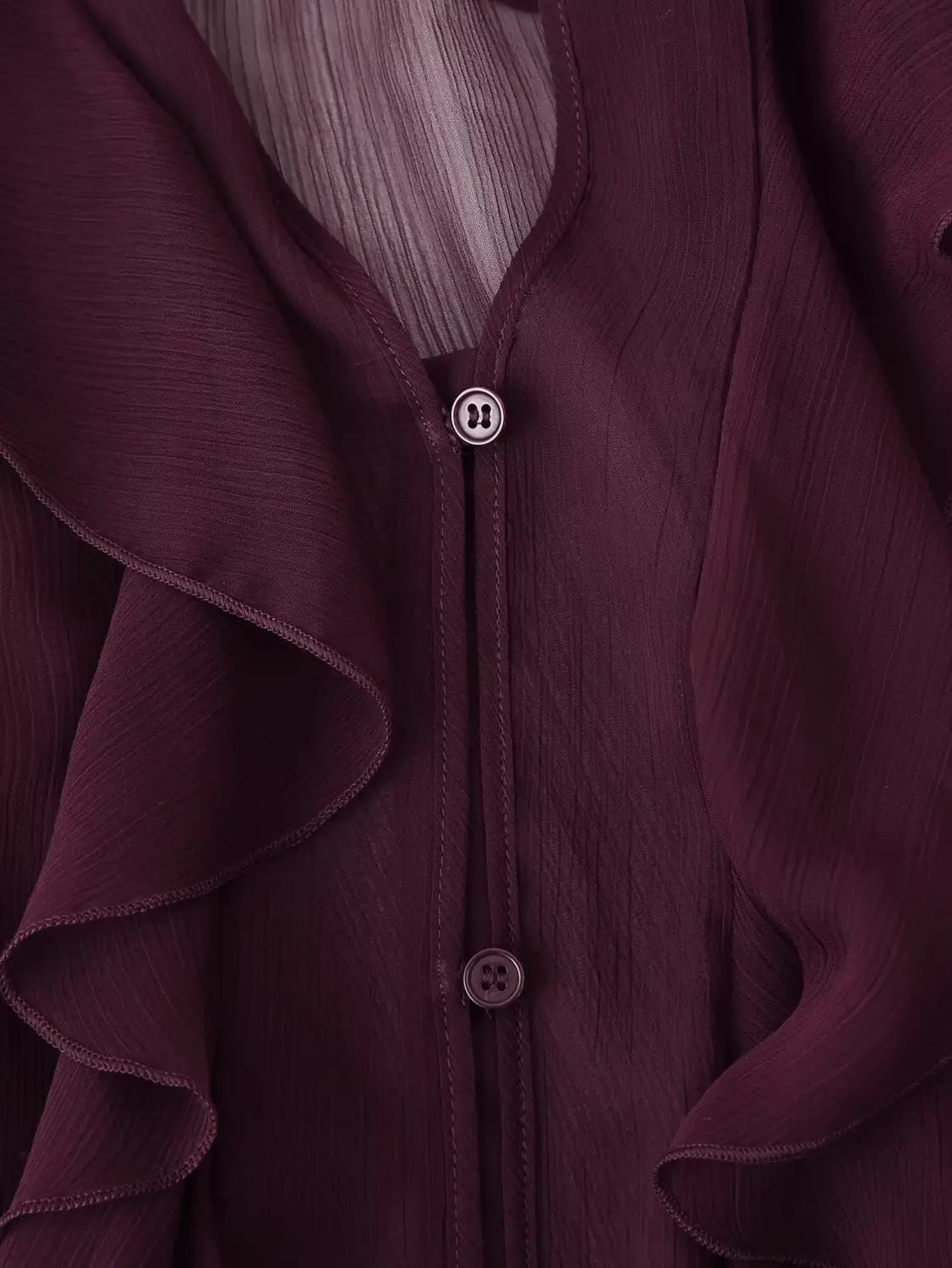A deep burgundy long sleeve ruffle shirt long made of chiffon with a v-neck, subtle sheen, matching buttons, and delicate pleated detailing.