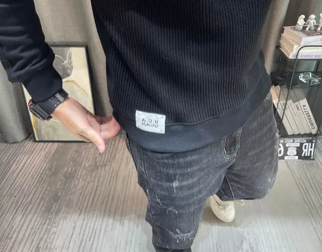 Pull-over en maille à empiècement contrastant pour homme, manches longues, en tissu noir en maille côtelée, avec une étiquette de marque rectangulaire blanche sur la ceinture.