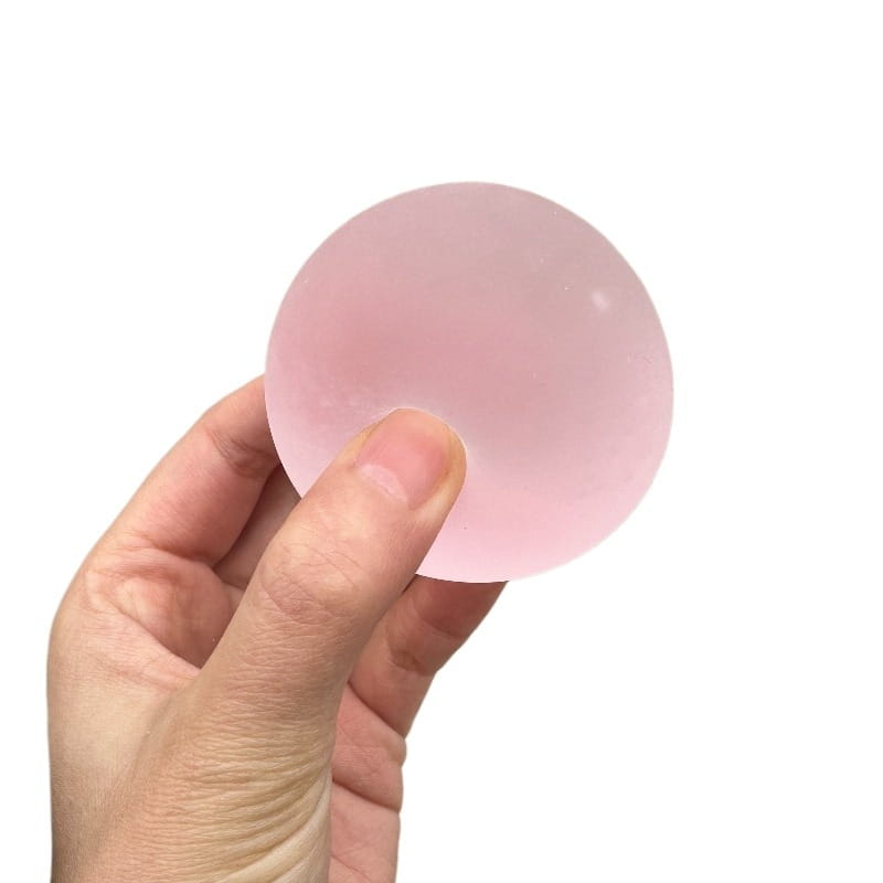 a translucent pink spherical stress ball made of soft mochi material held in a hand designed as a sensory fidget toy.