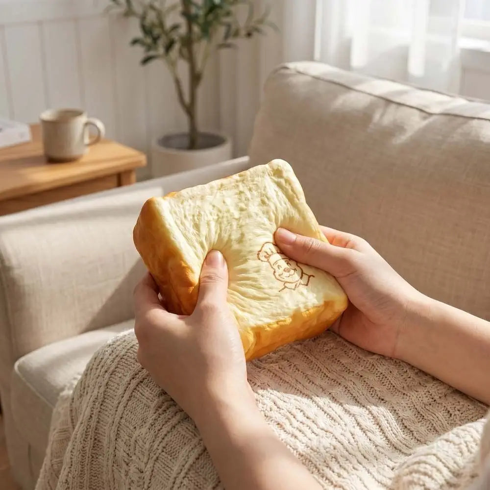 a soft squishy toy shaped like bread with a golden-brown crust and pale yellow interior featuring a cute cartoon character embroidered on top, designed as a chef bread fidget toy suitable for a universal age range
