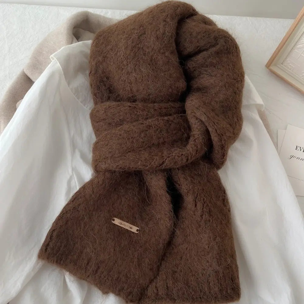 Una bufanda de punto de invierno para mujer marrón, hecha de una tela de punto suave y esponjosa con textura, con un diseño de calentador de cuello tipo chal cálido y una pequeña etiqueta metálica en el extremo.