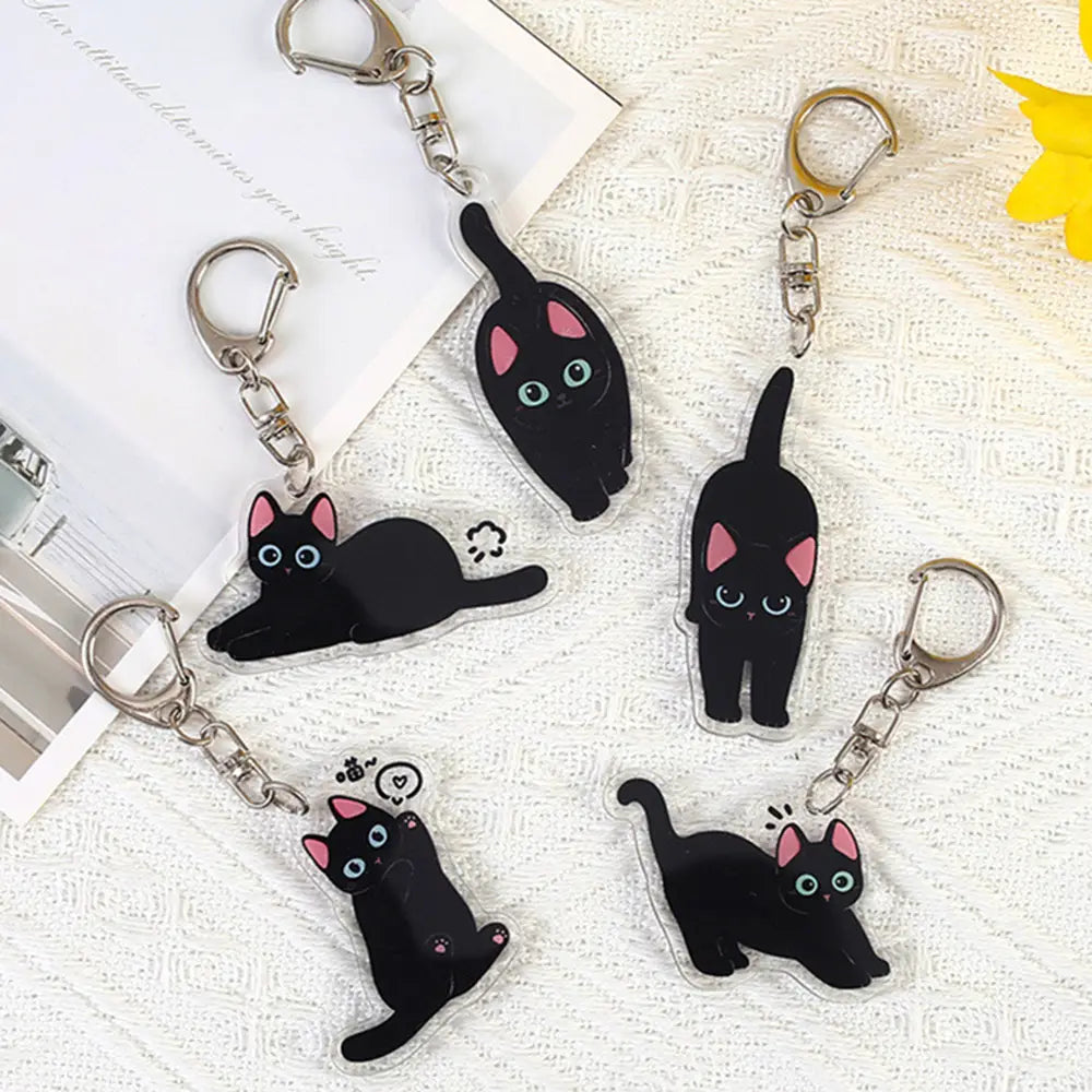 Clear acrylic black cat keychains with pink inner ears and light blue eyes in various poses designed as cartoon animal bag charms.