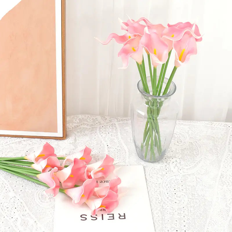 A bouquet of pink artificial calla lilies with yellow centers arranged in a clear glass vase for home decor.