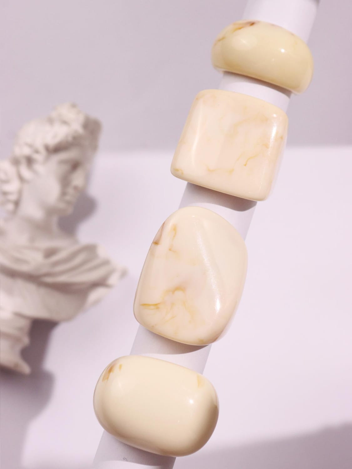 Cream-colored polished amber beads in various shapes including rounded and square featured in a chunky resin cocktail rings 4-piece set.