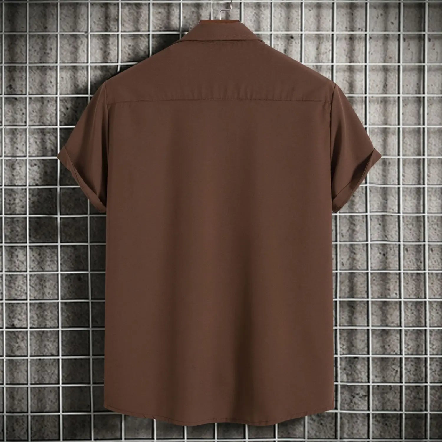 Chemise marron à manches courtes pour homme, avec col classique et coutures soignées, affichée sur un cintre contre un arrière-plan à motif quadrillé, idéale pour des chemises de plage et des looks décontractés unis pour hommes.