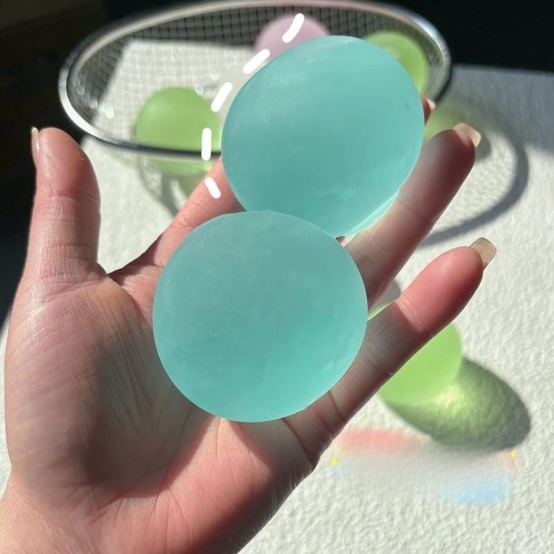 A hand holding two translucent light blue gel balls of the Blue Mochi Squeeze sensory fidget toy.