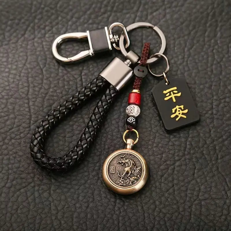 中国の干支をモチーフにした編みレザー製ラッキーペンダントのコレクションより。ブロンズの「龍」メダリオン、シルバートーンの留め金およびリングを備え、赤と白のビーズでアクセントを施した黒の編みレザー製キーチェーン。金色の漢字が刻まれた黒いタグ付き。