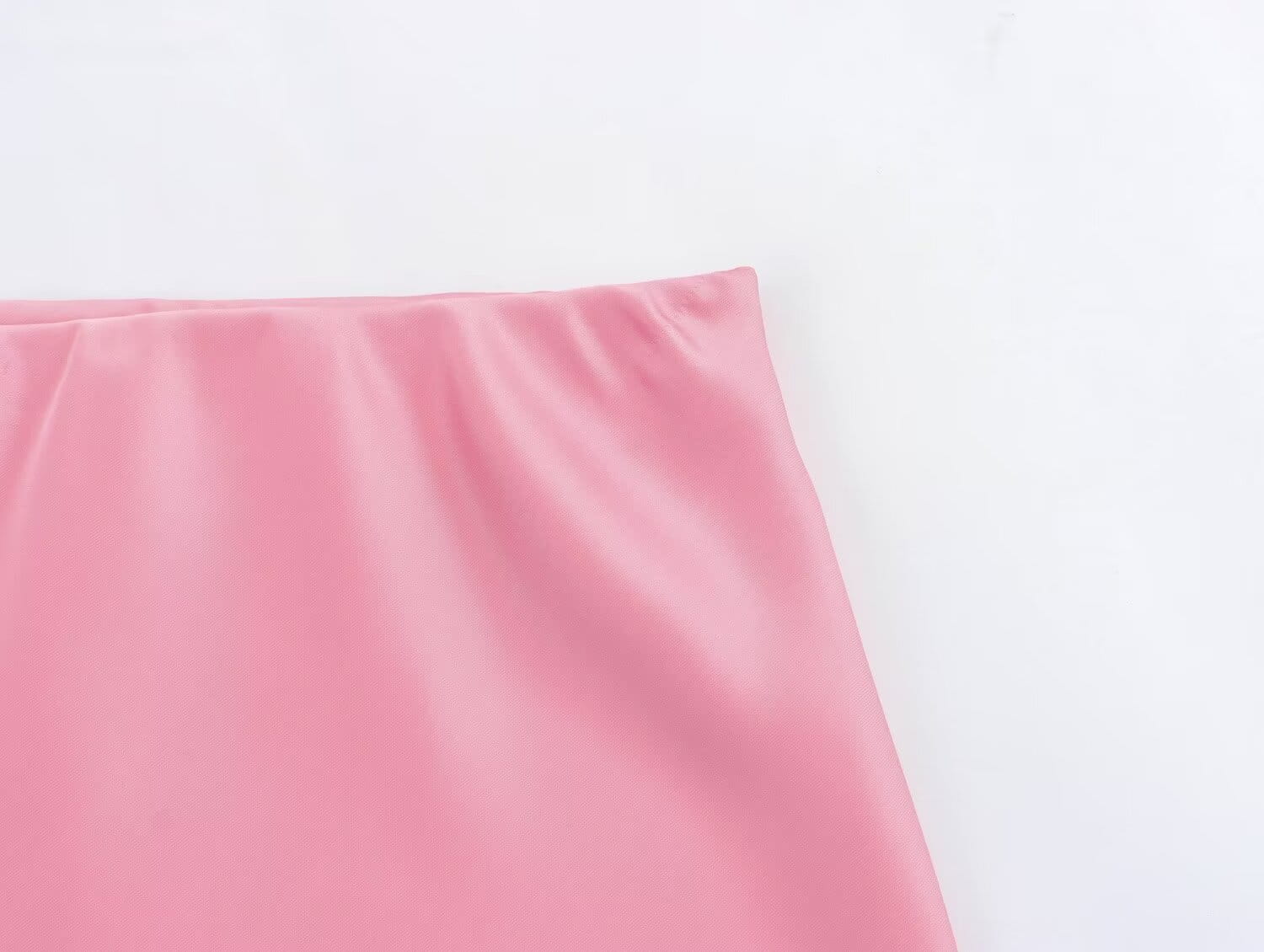 Une jupe midi en satin rose tendre, à taille haute, finition lisse et brillante, et plis délicats sur l’ourlet, conçue comme une longue jupe élégante.