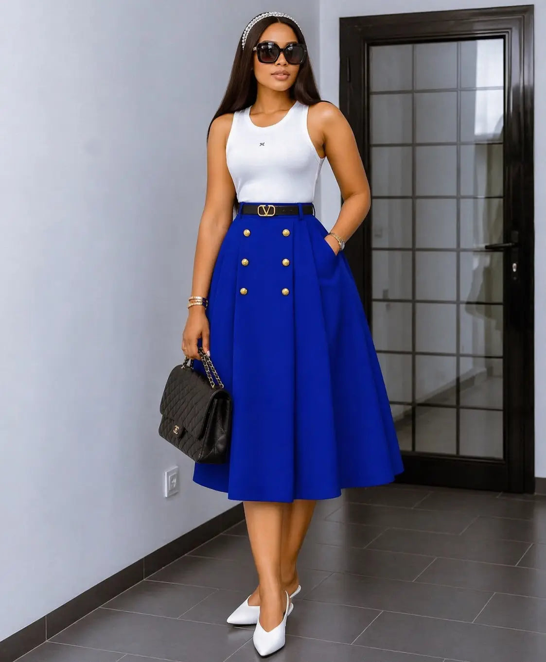 Une femme portant une jupe midi en maille à taille haute bleu royal éclatant, avec des boutons ton or et une ceinture noire assortie.