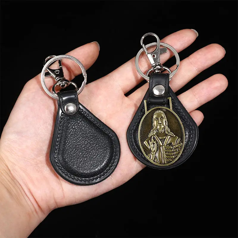Black leather Saint Christopher keychain with silver-toned metal clasp and gold-tone oval medallion featuring a religious figure in antique bronze finish.