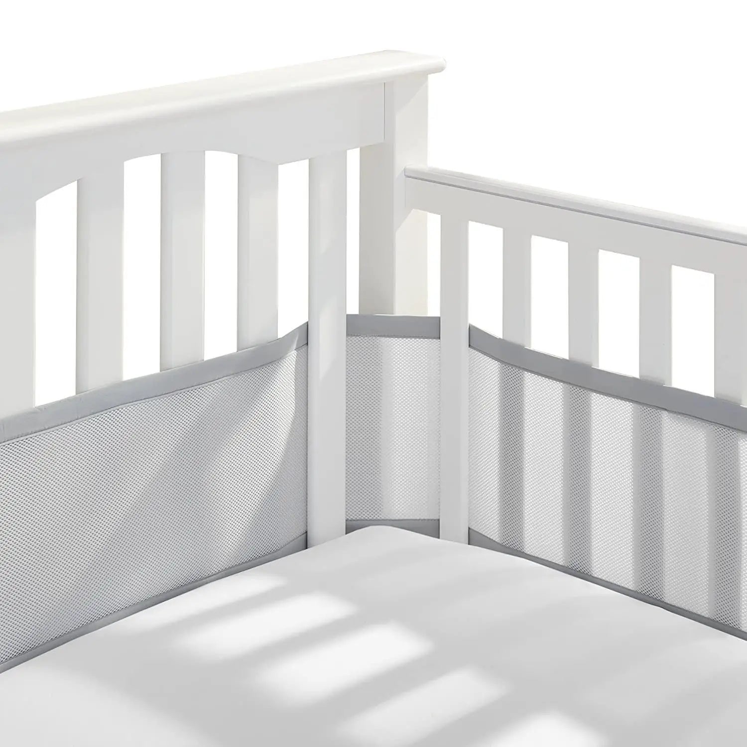 Grauer atmungsaktiver Mesh-Krippenstoßschutz mit grauem Einfassungsrand, innerhalb eines Kinderbetts mit weißen Holz-Lamellen für Teddy-Bären-Bettwäsche montiert.