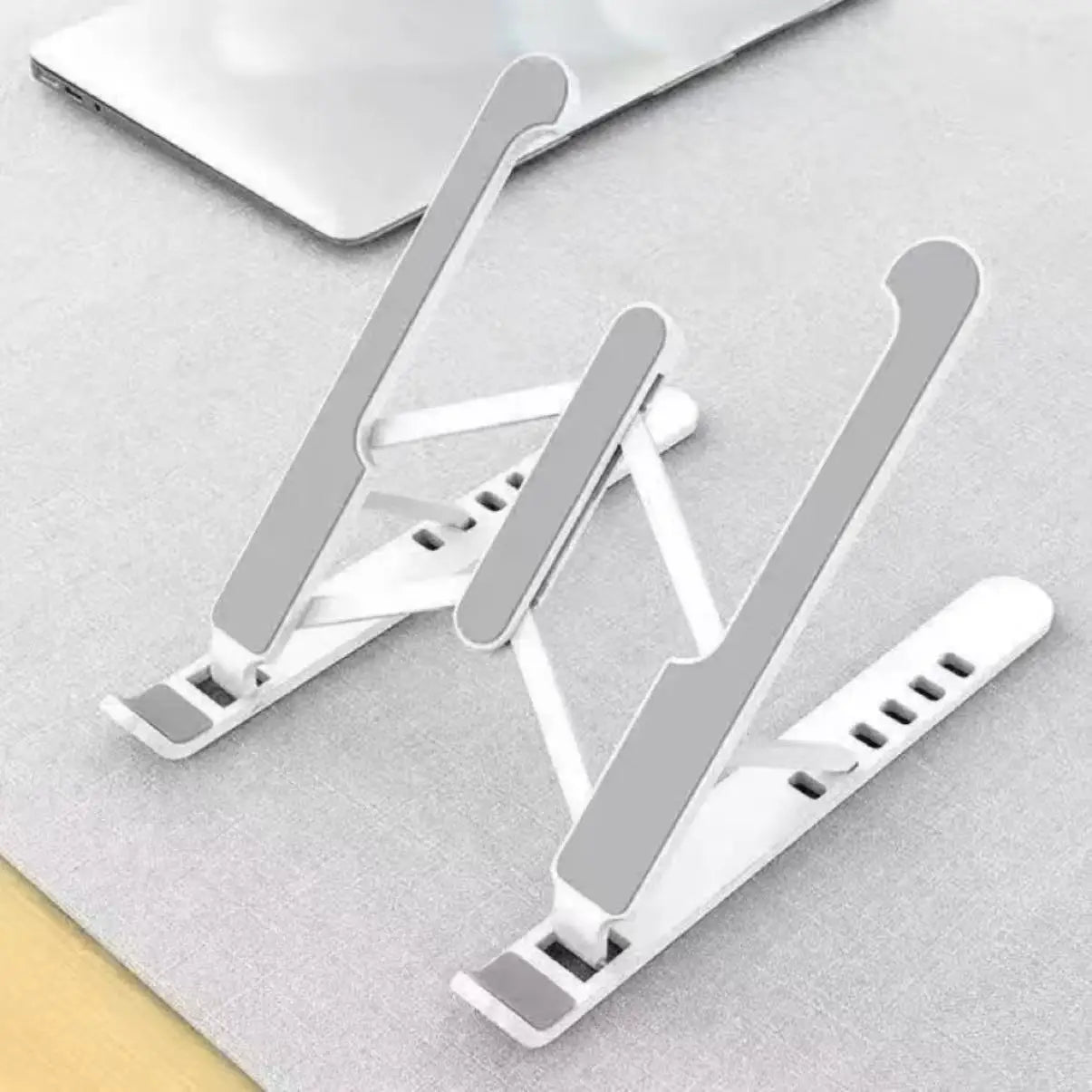 Support d’ordinateur portable blanc et argent pliable et réglable, doté d’un design minimaliste élégant pour un usage ergonomique.