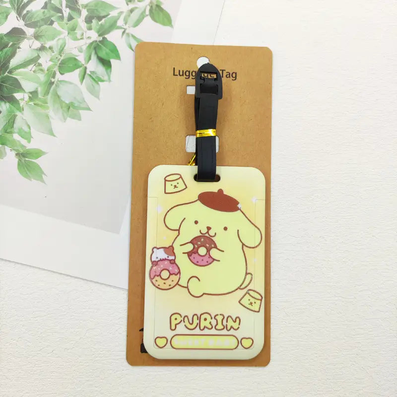 Étiquette de bagage rectangulaire Hello Kitty jaune pâle, représentant un personnage Purrin en dessin animé portant un béret rouge et tenant des beignets, fixée à une sangle noire avec une attache métallique de couleur dorée.