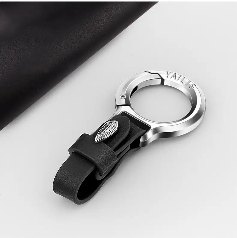 Lederschlüsselanhänger für den Pkw, mehrzweckiger Anti-Verlust-Halter, mit schwarzem Lederriemen, silberner Metallklemme und Logo, befestigt an einem eleganten Edelstahl-Schlüsselring.