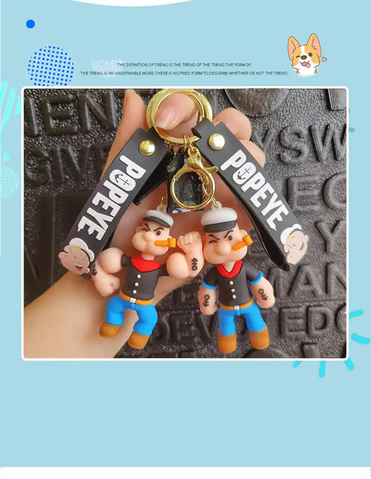 Black and gold popeye silicone keychain with molded plastic figure wearing a sailor outfit used as a cartoon doll bag pendant.