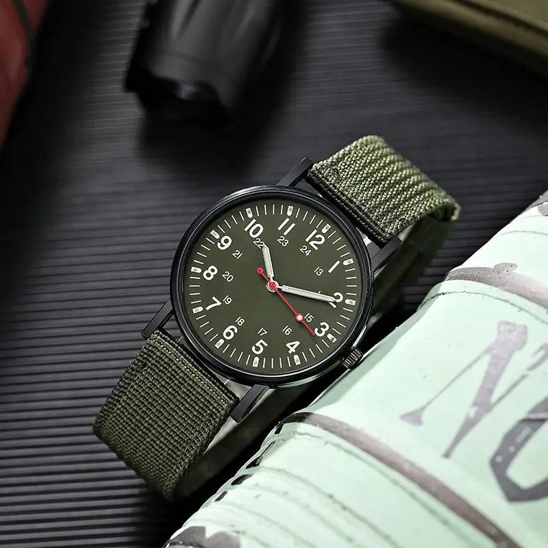 Militärisches Quarzarmbanduhr mit olivgrünem Nylonarmband, schwarzem Gehäuse und dunklem Zifferblatt mit weißen Ziffern.