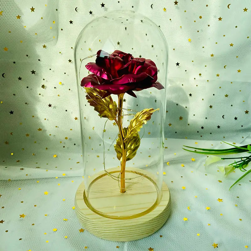 Eine metallische Rose mit tiefroten Blütenblättern und goldenen Blättern, dargestellt in einer klaren Glaskuppel mit LED-Licht auf einem hellen Holzsockel, mit dem Titel „Eternal Gold Rose Glass Dome Led Light Gift“.