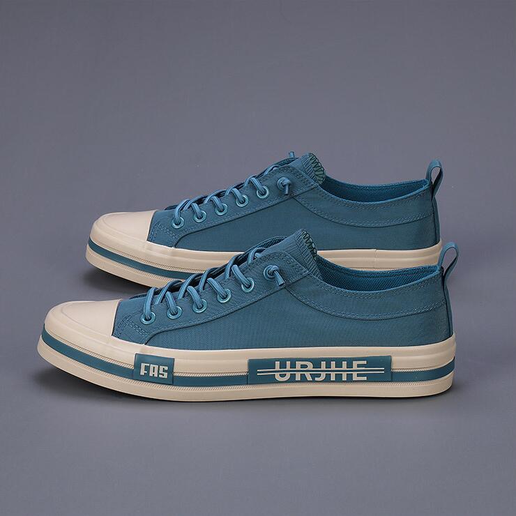 Baskets décontractées en toile pour hommes, chaussures d’été légères en bleu sarcelle, avec des semelles en caoutchouc blanc, des lacets assortis, et une bande d’inscription noire audacieuse sur le côté.
